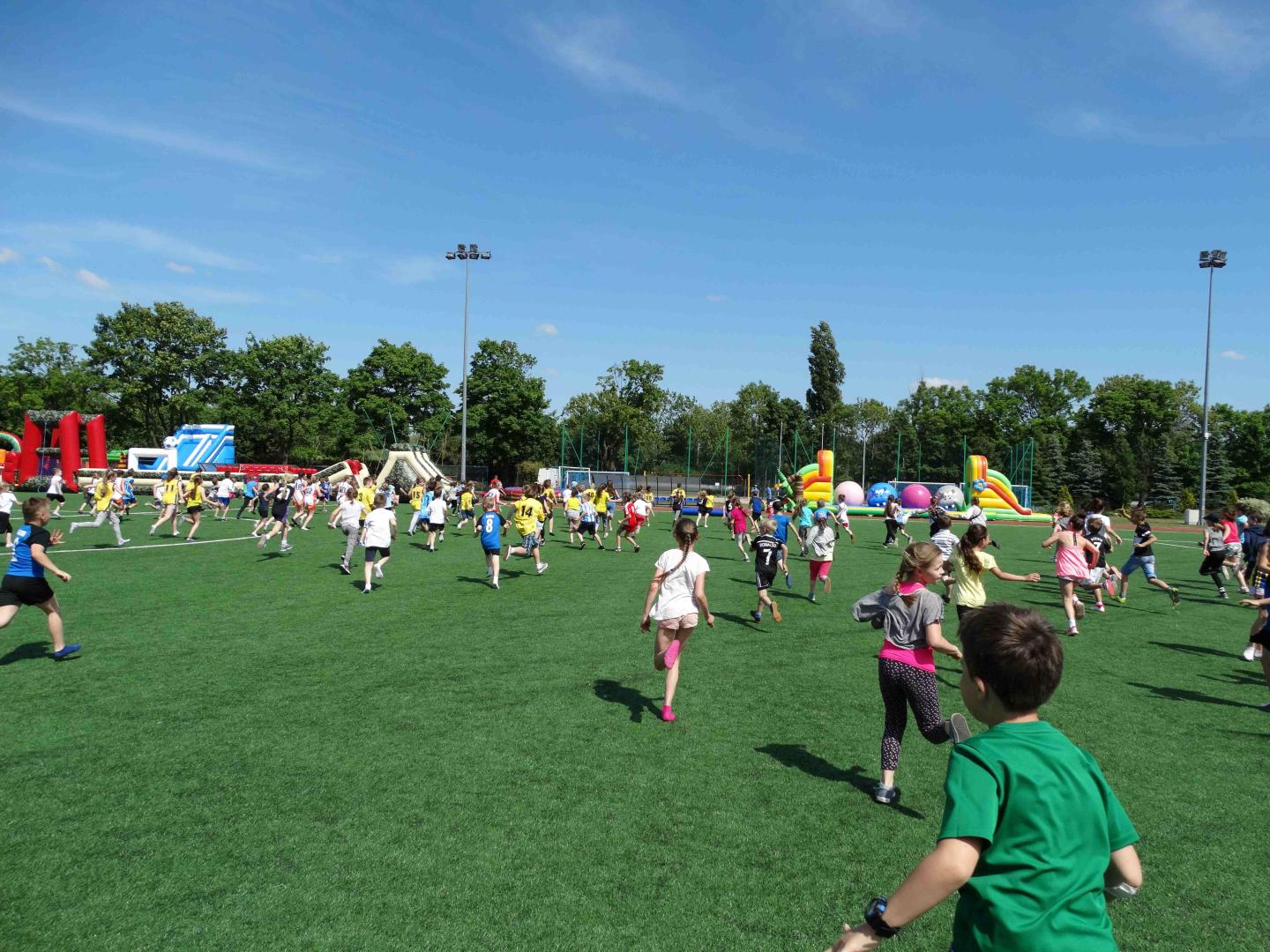 Dzieci na boisku MOS, fot. Adam Ciereszko - dzieci biegną pod boisku, a w tle widać kolorowe dmuchańce - grafika artykułu