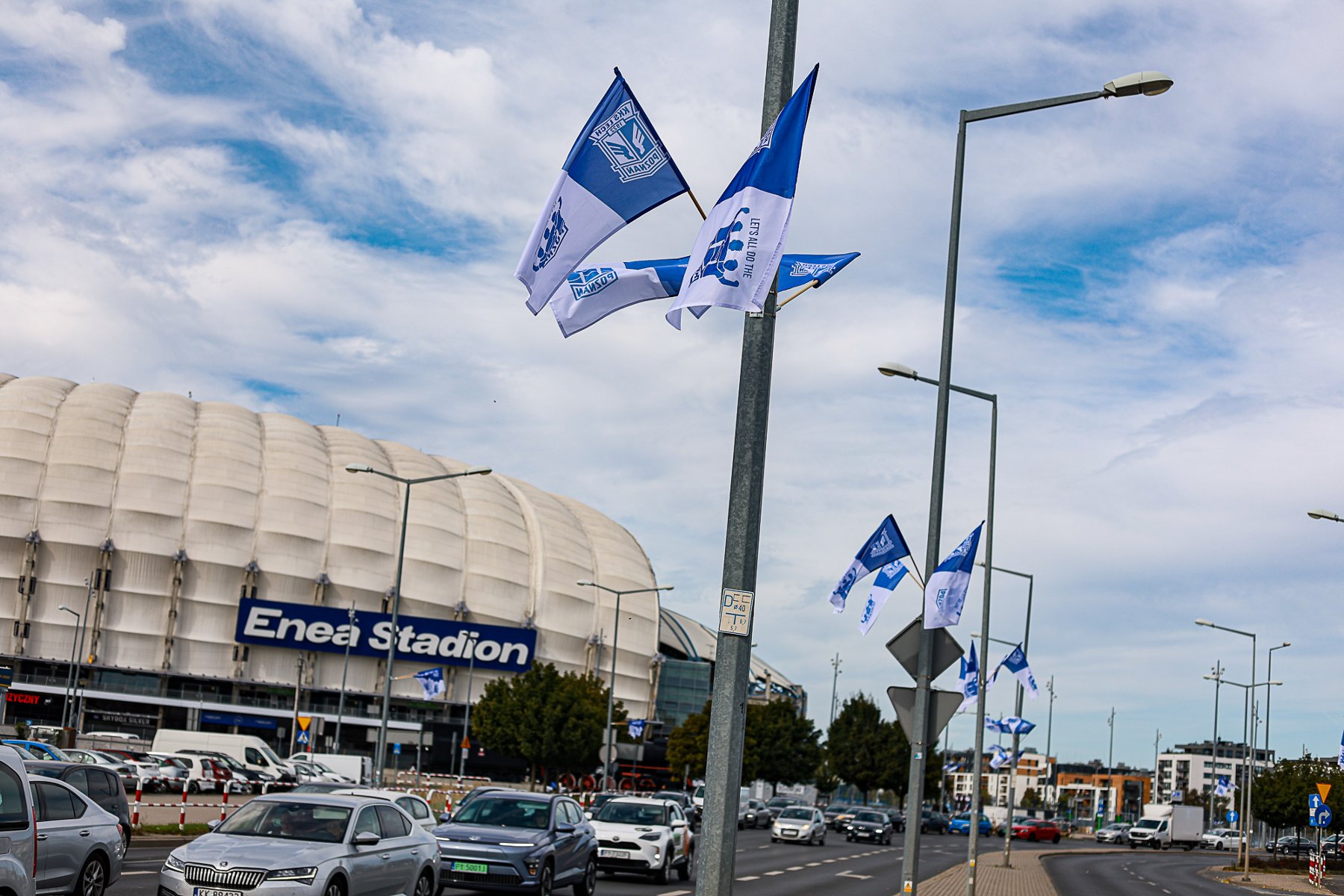 Flagi Lecha na latarniach. W tle stadion - grafika artykułu