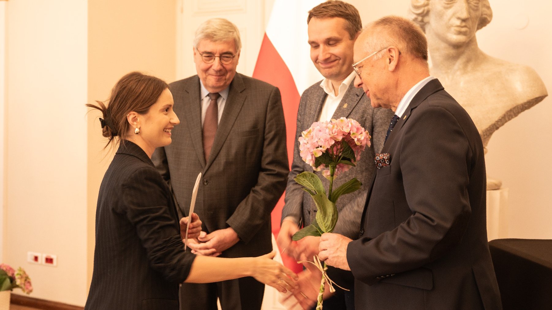 trzej mężczyzn wręcza dyplom i kwiata kobiecie