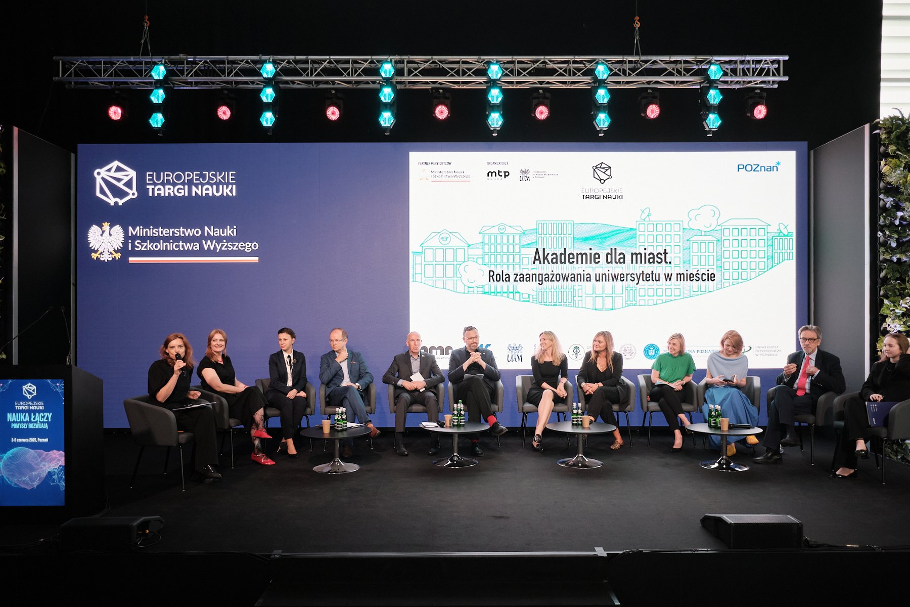 Zdjęcie przedstawia grupę panelistów i panelistek siedzących na scenie, na tle prezentacji wyświetlanej na dużym ekranie - grafika artykułu