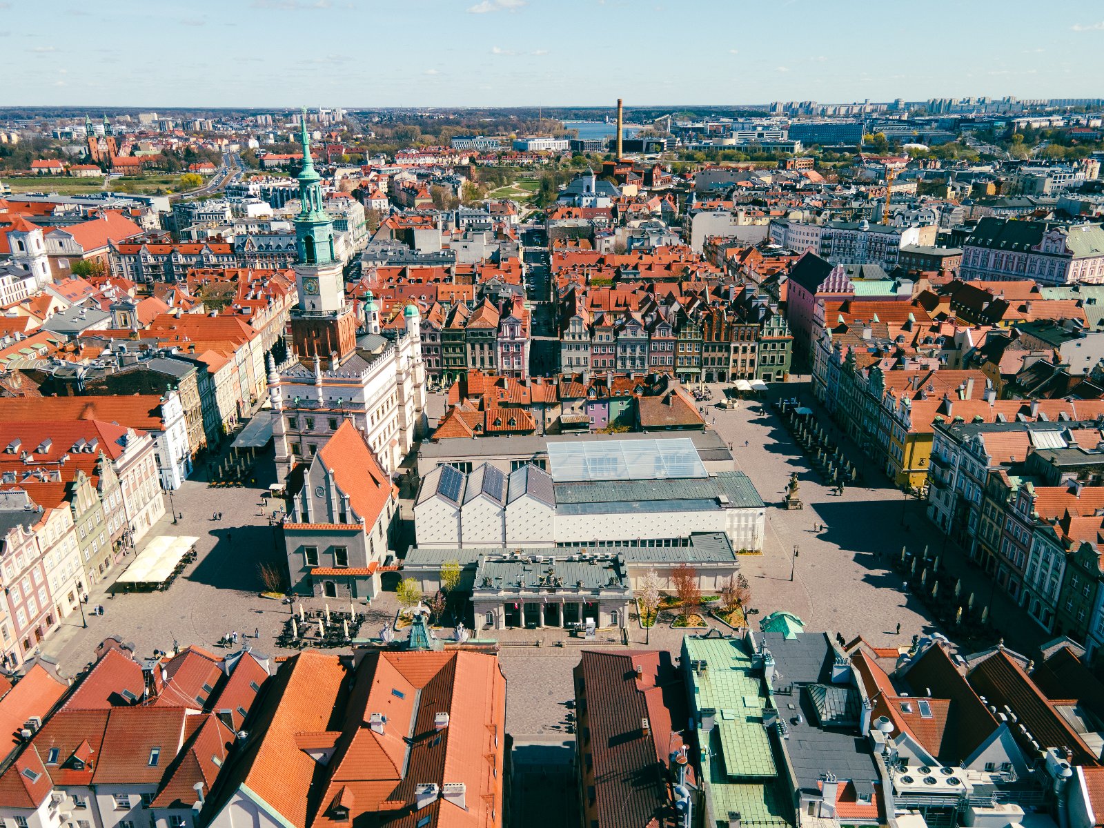 Widok z lotu ptaka na centrum miasta. W centrum rozległy plac otoczony budynkami z czerwonymi dachami. Na placu charakterystyczny budynek z zieloną wieżą, prawdopodobnie obiekt historyczny. - grafika artykułu