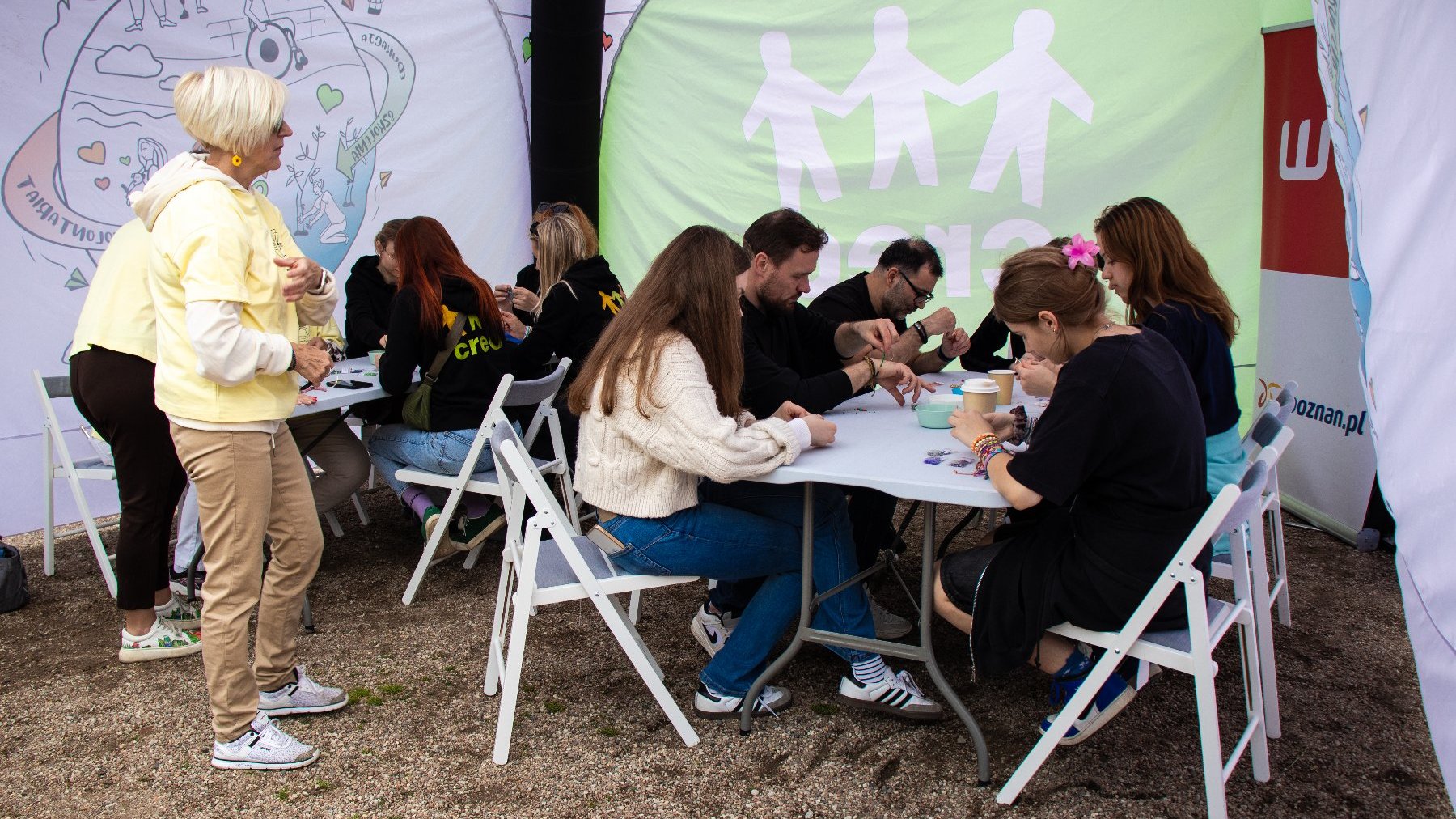 Na zdjęciu widać grupę osób siedzących przy stołach znajdujących się pod namiotem.