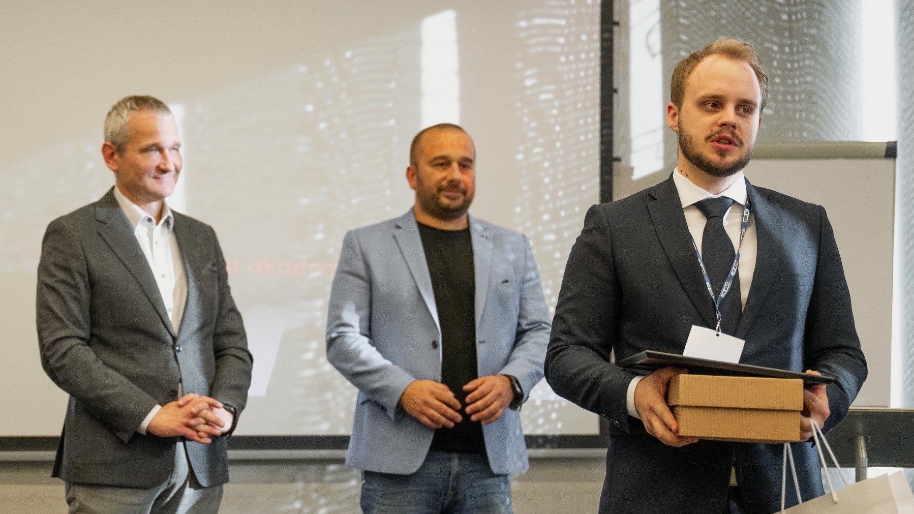 Na zdjęciu trzej mężczuźni w garniturach, jeden z nich coś mówi