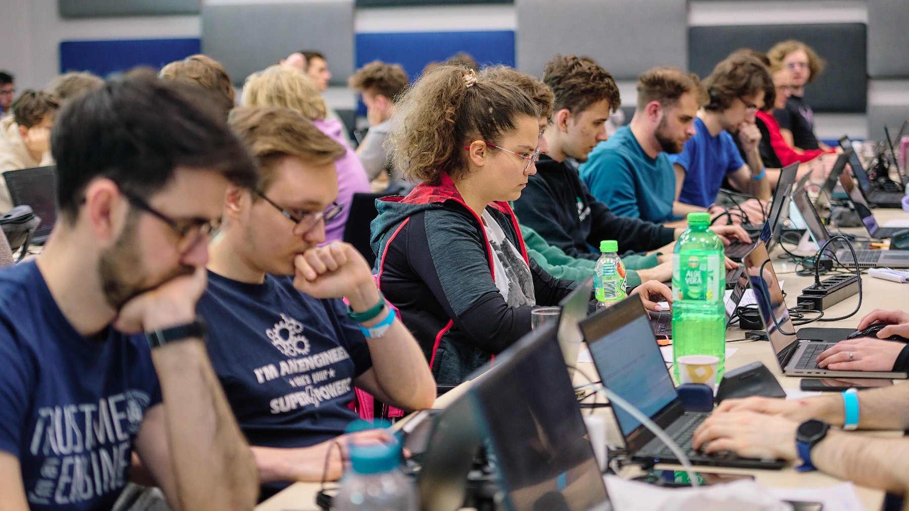Grupa osób siedzi przy komputerach. Programują w zamyśleniu.