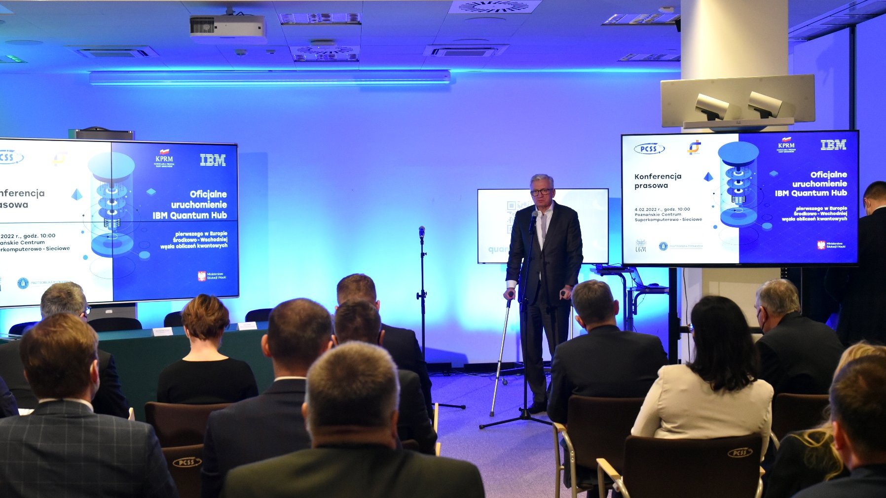 Zdjęcie przedstawia przemawiającego na środku sali prezydenta Poznania oraz słuchających go ludzi siedzących na krzesłach.