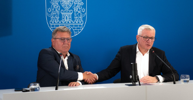 Na zdjęciu dwóch mężczyzn za stołem konferencyjnym ściskających ręce