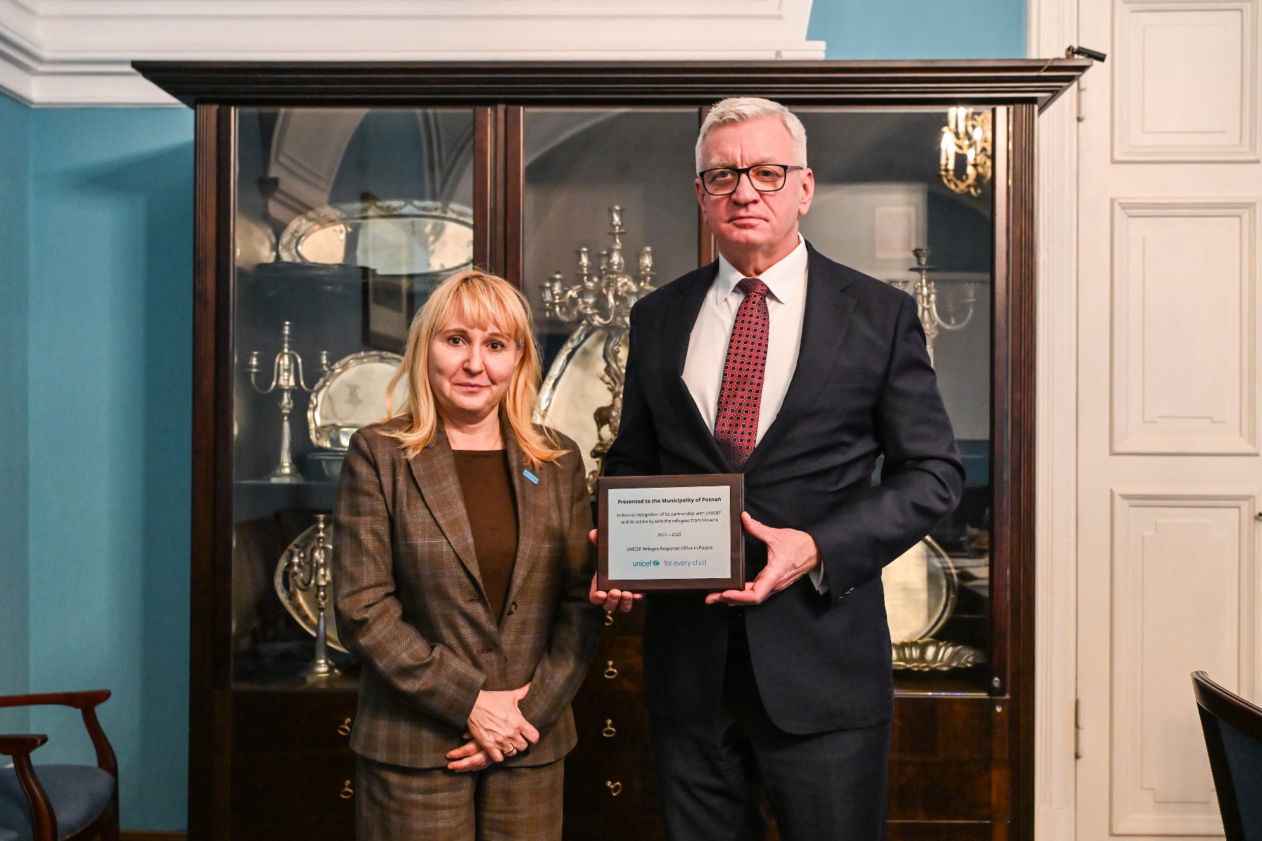 Na zdjęciu mężczyzna i kobieta pozują do obiektywu, mężczyzna trzyma tabliczkę - grafika artykułu