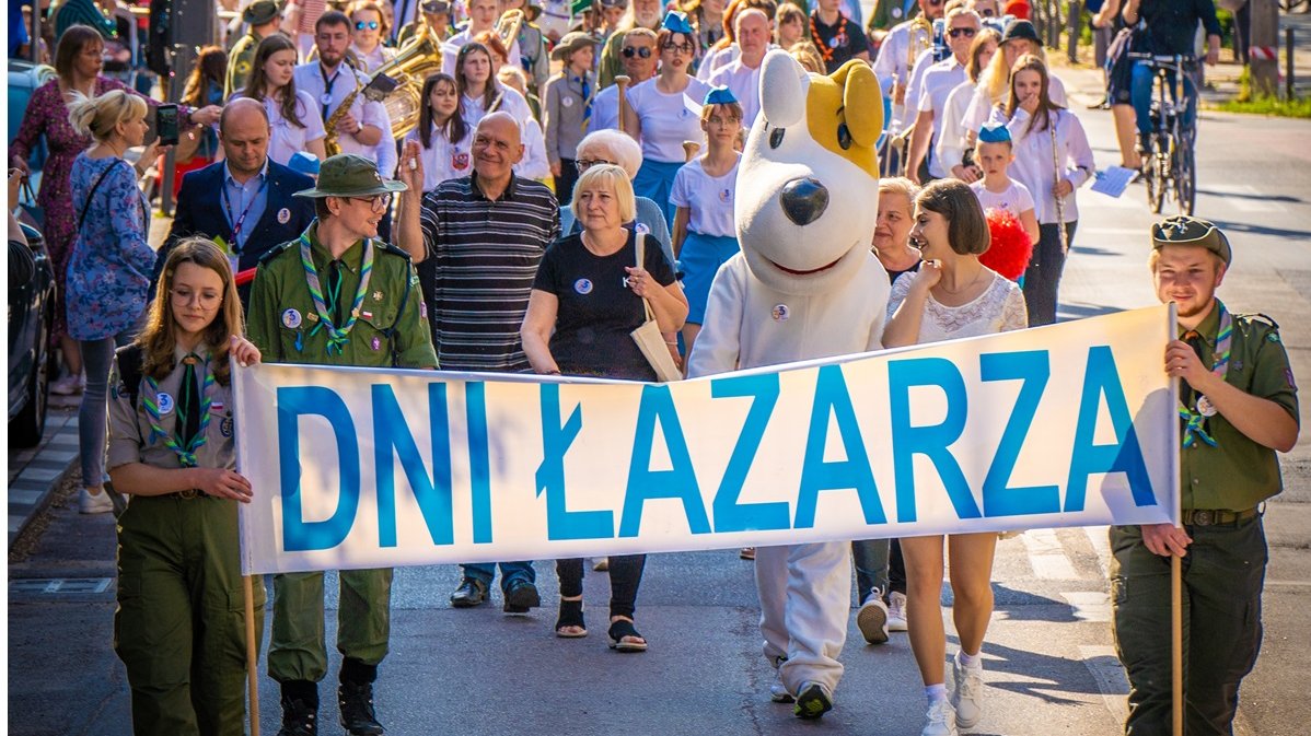 Parada mieszkańców Łazarza. Na czele przemarszu para harcerzy niesie transparent z napisem Dni Łazarza. Z nimi idą uczestnicy parady.
