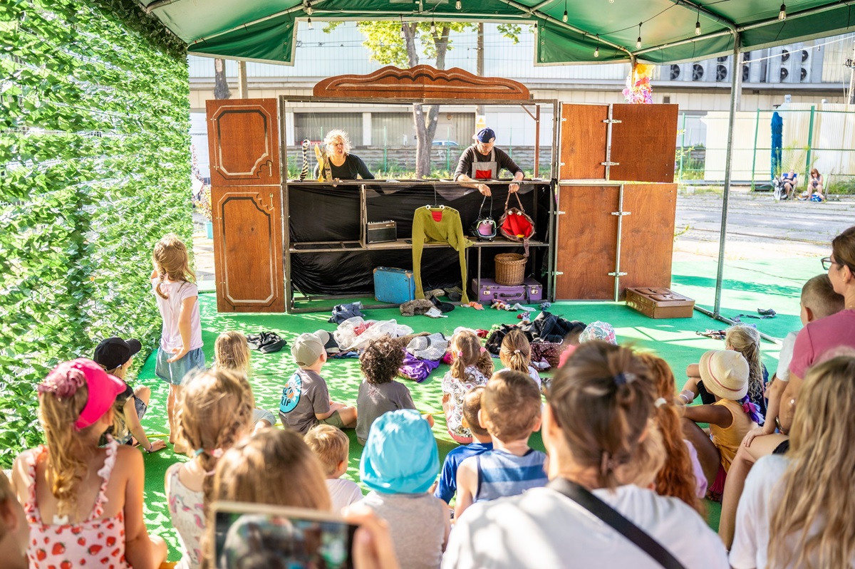 Dwójka aktorów występuje przed dziećmi. Stoją oni za rozkładanym drewniany prarawanem. Na jego tle odgrywają przedstawienie. - grafika artykułu