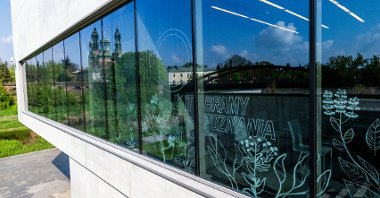 Przeszklona elewacja Bramy Poznania z odbijającymi się w szkle wieżami katedry, widoczny banner 10 lat Bramy Poznania