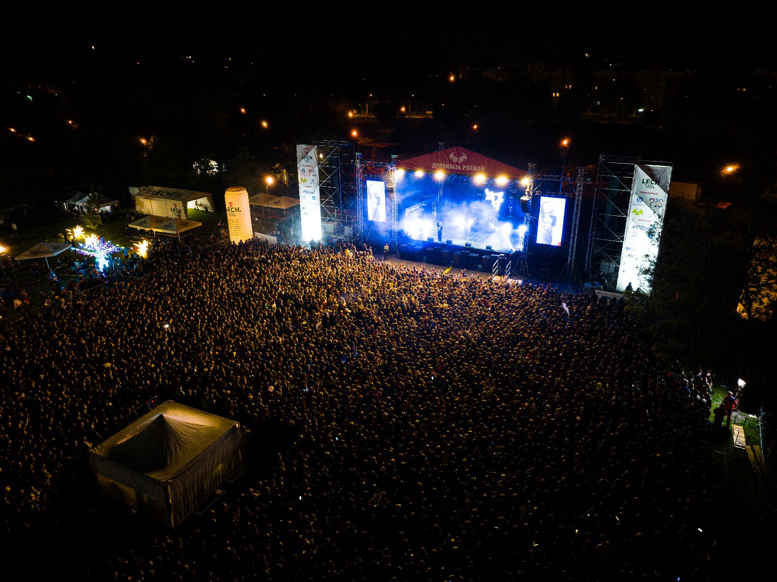 Zdjęcie z powietrza pokazujące tłum publiczności zgromadzony przed sceną oświetloną światłami scenicznymi - grafika artykułu