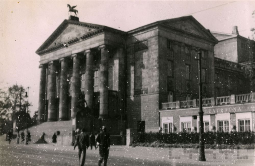 Czarno-białe zdjęcie Teatru Wielkiego w Poznaniu od frontu. Ulicą spacerują ludzie. Fotografia jest ziarnista, złej jakości. - grafika artykułu