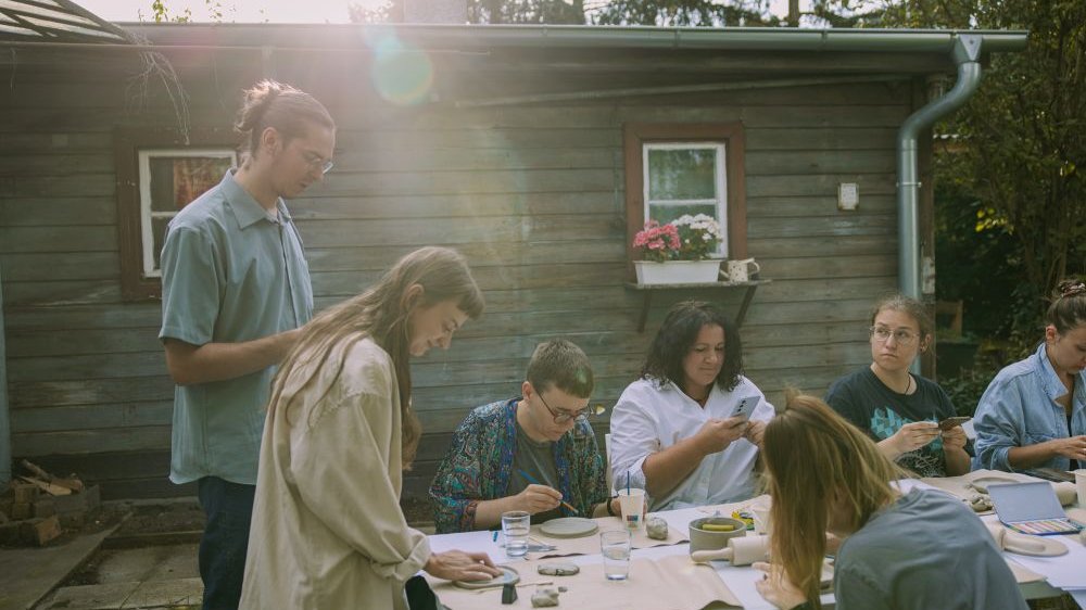 Uczestnicy warsztatów tworzą coś ręcznie na stole ustawionym na dworze.