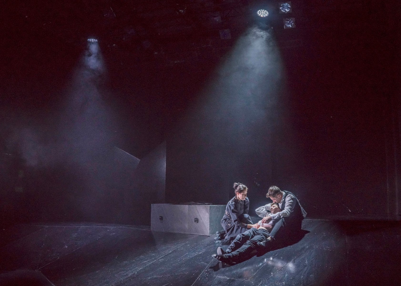 Ciemna scena. W centrum dwoje młodych ludzi kuca nad trzecin, który leży w mękach. - grafika artykułu