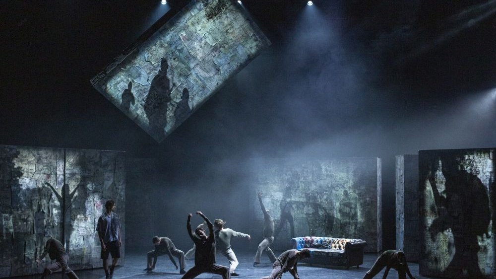 Tancerze w różnych pozach na scenie. Rzucają cienie.