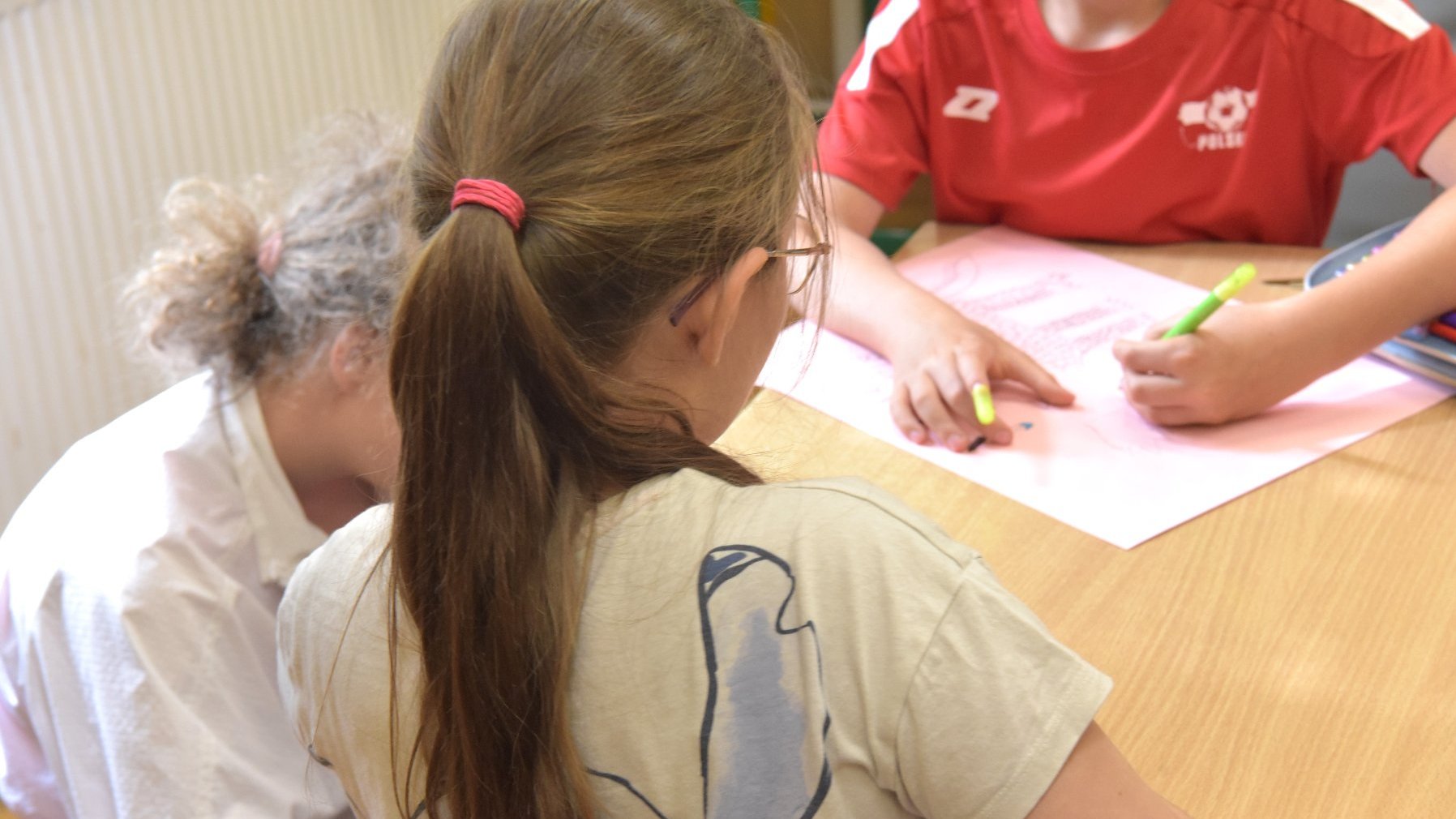 Zdjęcie przedstawia dzieci siedzace przy stole i rysujące.