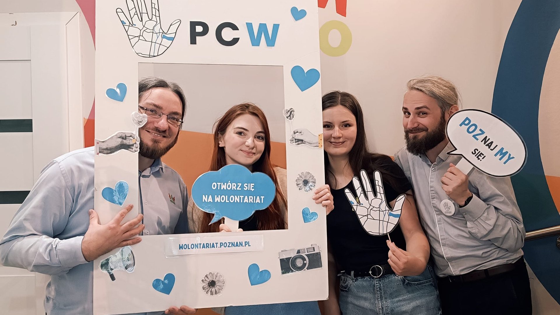 zdjęcie przedstawia uśmiechniętych pracowników Stowarzyszenia CREO - cztery osoby, w tym dwie kobiety i dwóch mężczyzn. Osoby trzymają w rękach ramkę do zdjęć oraz plakietki z napisami związanymi z wolontariatem