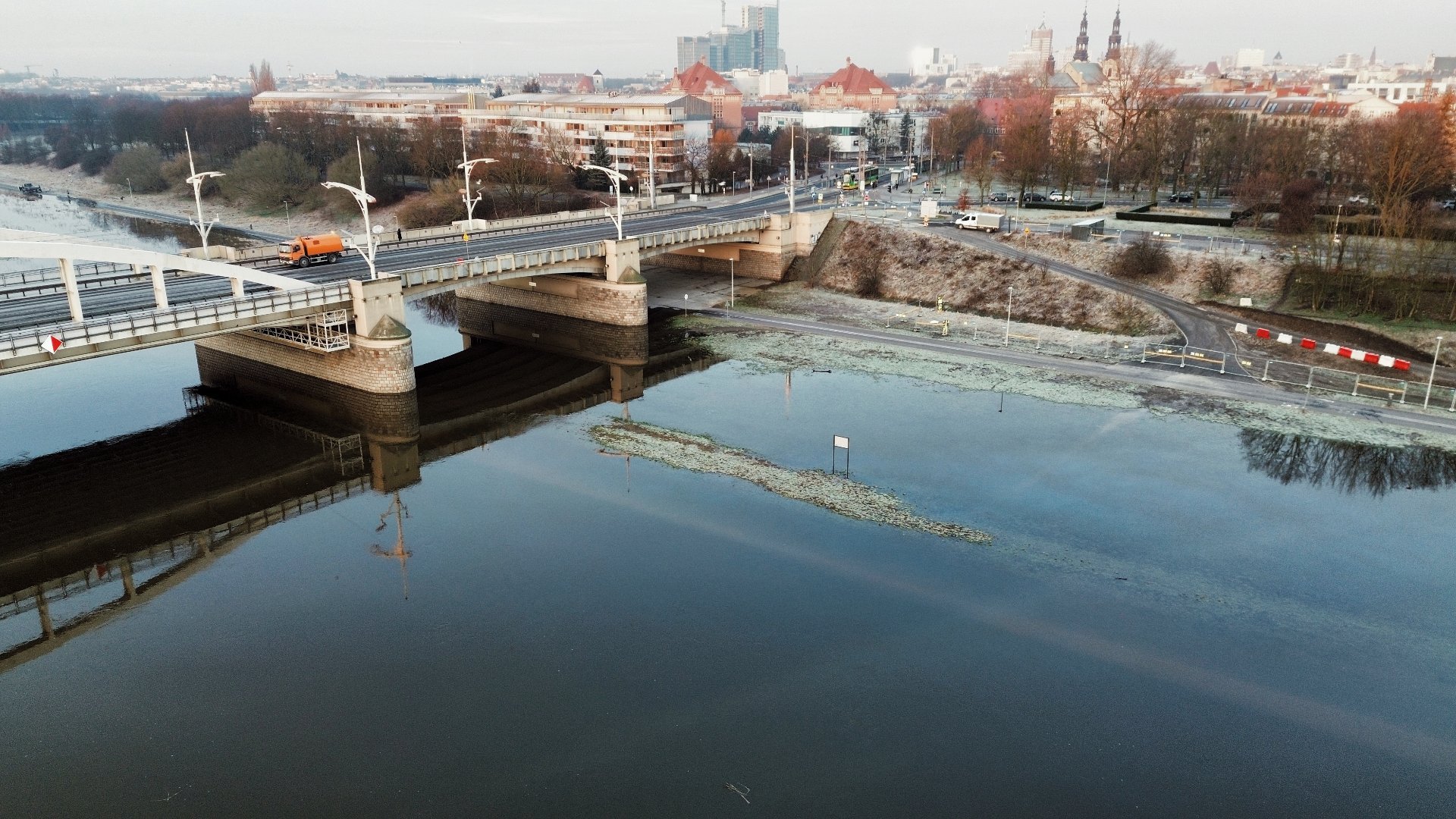 Widok z lotu dronem na most, i wały nadrzeczne, z których prowadzi droga nad rzekę. Widać wysoki poziom wód w rzece.