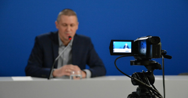 Zdjęcie przedstawia Patryka Pawełczaka, dyrektora Gabinetu Prezydenta UMP. Dyrektor siedzi za biurkiem, na pierwszym planie widać kamerę.