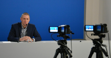 Zdjęcie przedstawia Patryka Pawełczaka, dyrektora Gabinetu Prezydenta UMP. Dyrektor siedzi za biurkiem, na pierwszym planie widać kamery.