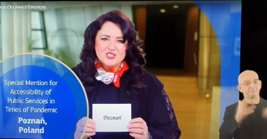 Screen: komisarz Helena Dali trzyma kartkę z nazwą zwycięskiego miasta: Poznań. Obok - tłumacz języka migowego