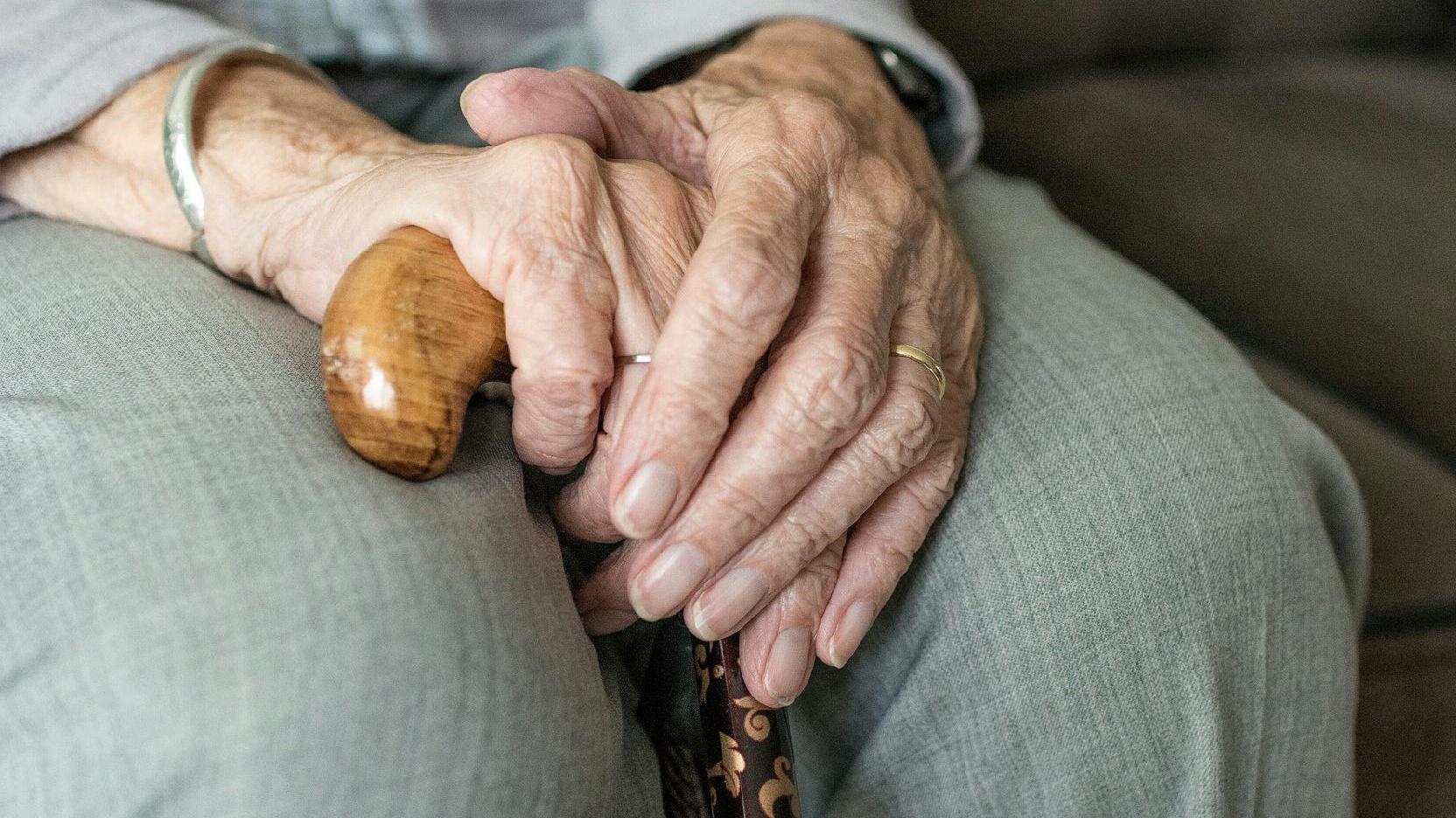 Zdjęcie: dłonie starszego człowieka, wsparte na kolanach, trzymające laskę - grafika artykułu