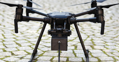 Zdjęcie przedstawia drona, stojącego na chodniku. Wykonano duże zbliżenie.