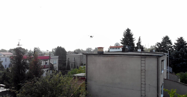 Zdjęcie przedstawia budynki jednorodzinne, nad którymi unosi się dron.