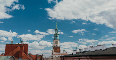 Panorama Poznania, na pierwszym planie dachy kamienic, w centrum wieża Ratusza, u góry błękitne niebo, na nim białe chmury