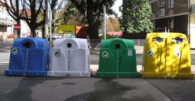 Na zdjęciu cztery różnokolorowe pojemniki na odpady stojące w rzędzie obok siebie