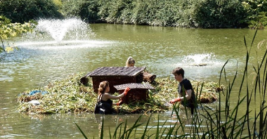 Zdjęcie przedstawia montaż pływających ogrodów. Widać na nim ludzi prowadzących te prace w wodzie.