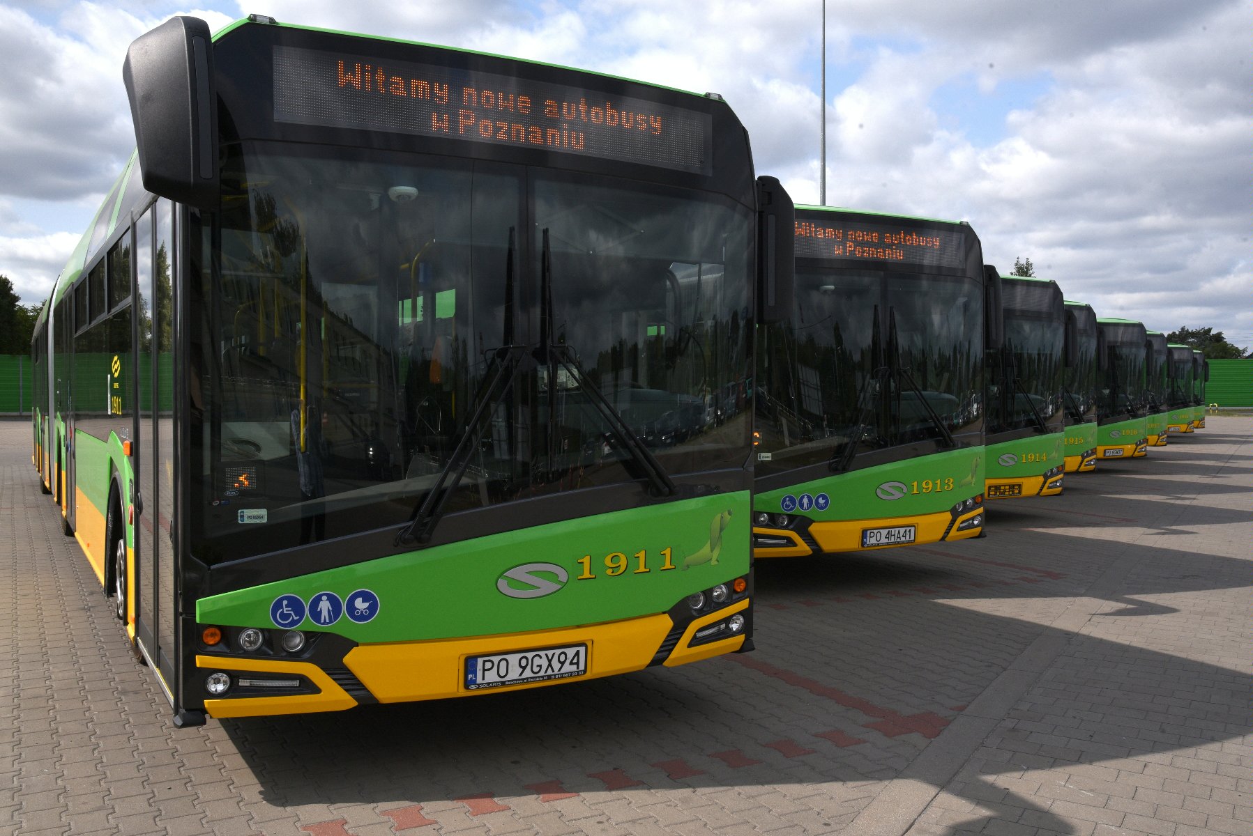Zdjęcie przedstawia 8 przegubowych autobusów niskopodłogowych, wykorzystywanych przez Miejskie Przedsiębiorstwo Komunikacyjne w Poznaniu. Pojazdy ustawione są pod kątem na parkingu, dzięki czemu możliwa jest ich prezentacja. - grafika artykułu