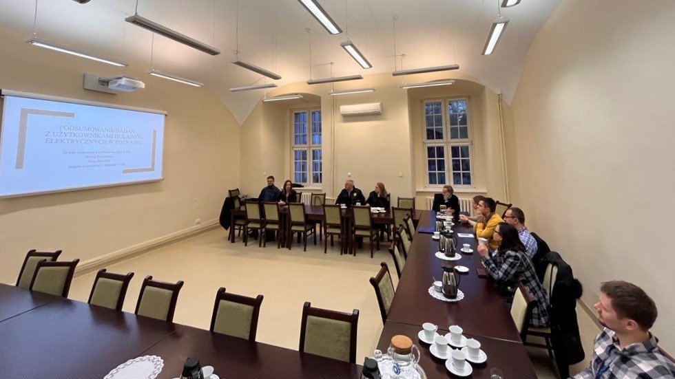 Zdjęcie sali, na której odbywa się zebranie. Kilka osób siedzi przy stołach, na których znajduje się kawa. Na jednej ze ścian projektor wyswietla prezentację. - grafika artykułu
