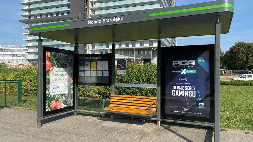 Wiata przystanku autobusowego z ławką i tablicą informacyjną oraz plakatami reklamowymi.