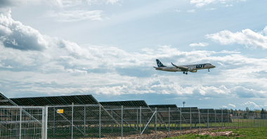 Na zdjęciu panele wotowoltaiczne, nad nimi leci samolot