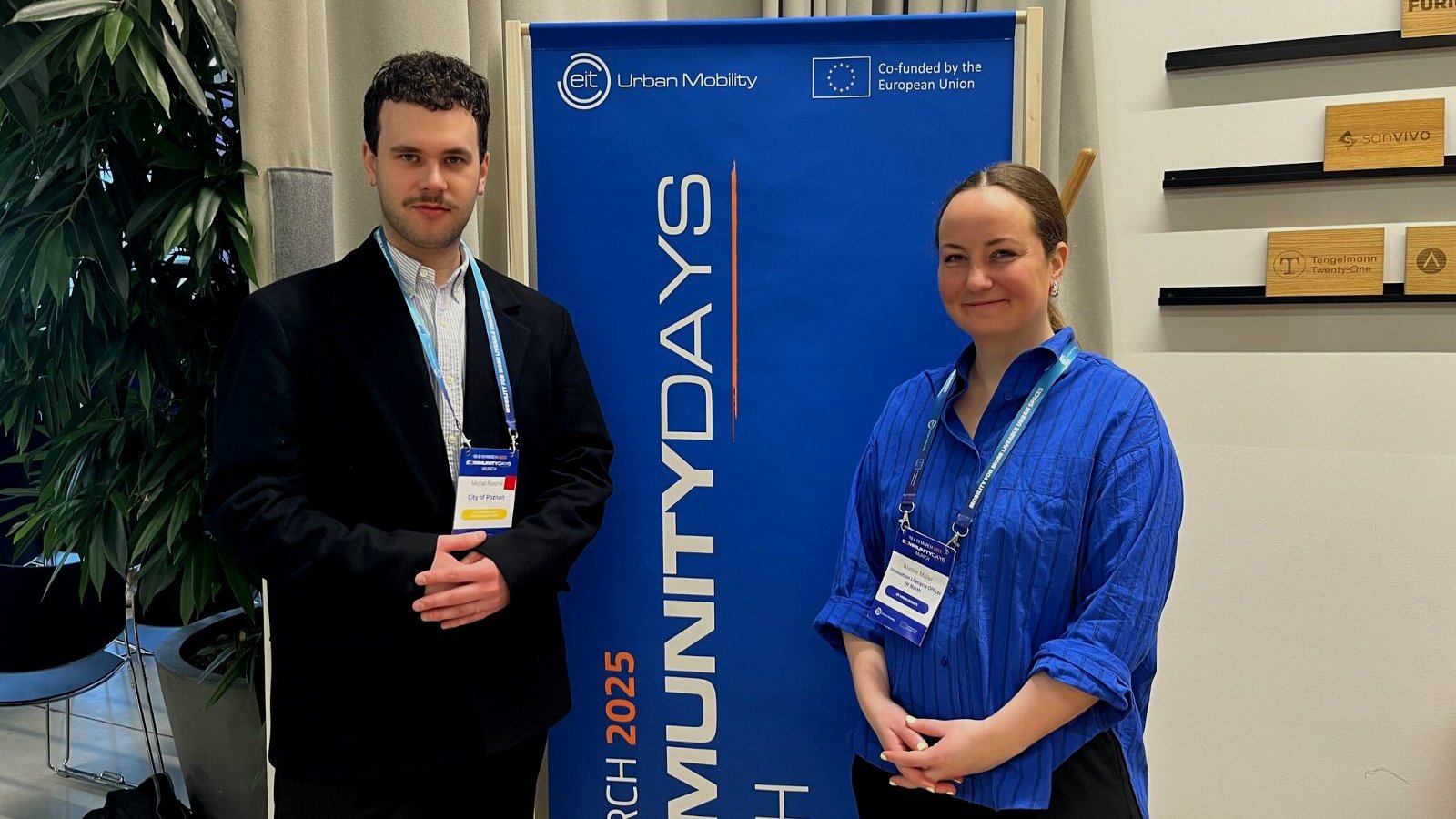 Na zdjęciu dwie osoby, uczestnicy wydarzenia, w tle baner z napisem CommunityDays Munich, EIT Urban Mobility, co-funded by European Union.