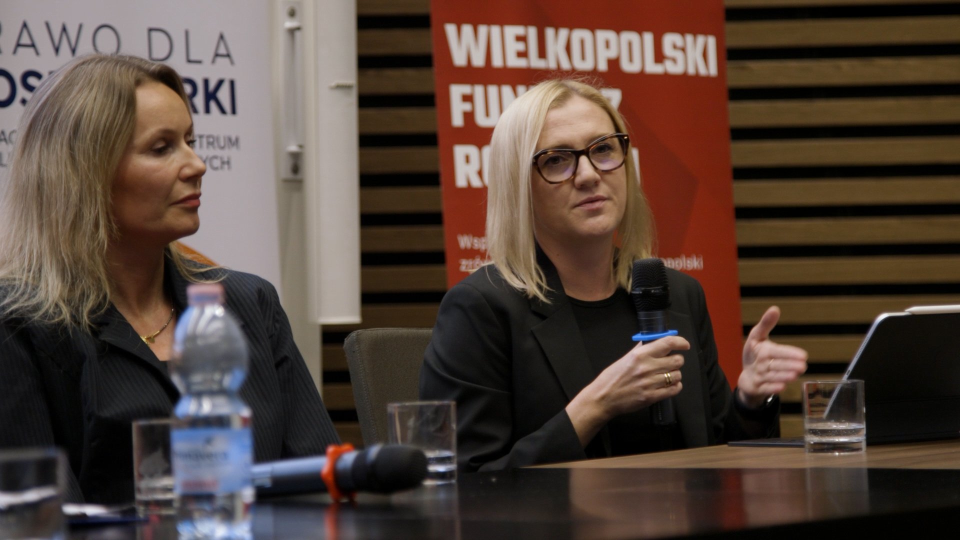Dwie kobiety siedzą za konferencyjnym stołem.