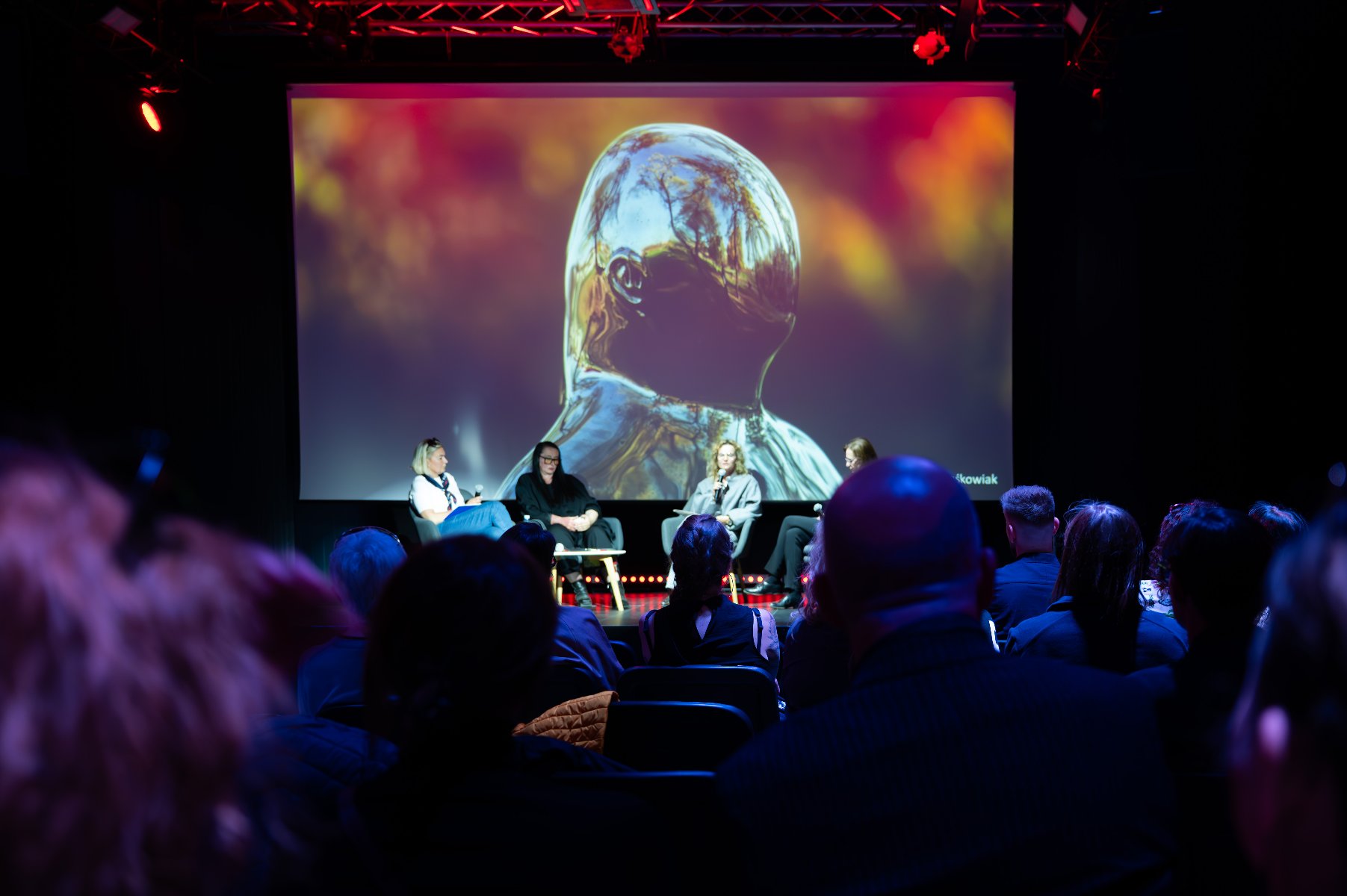 Na scenie siedzą cztery kobiety. Sala w ciemnych kolorach. - grafika artykułu