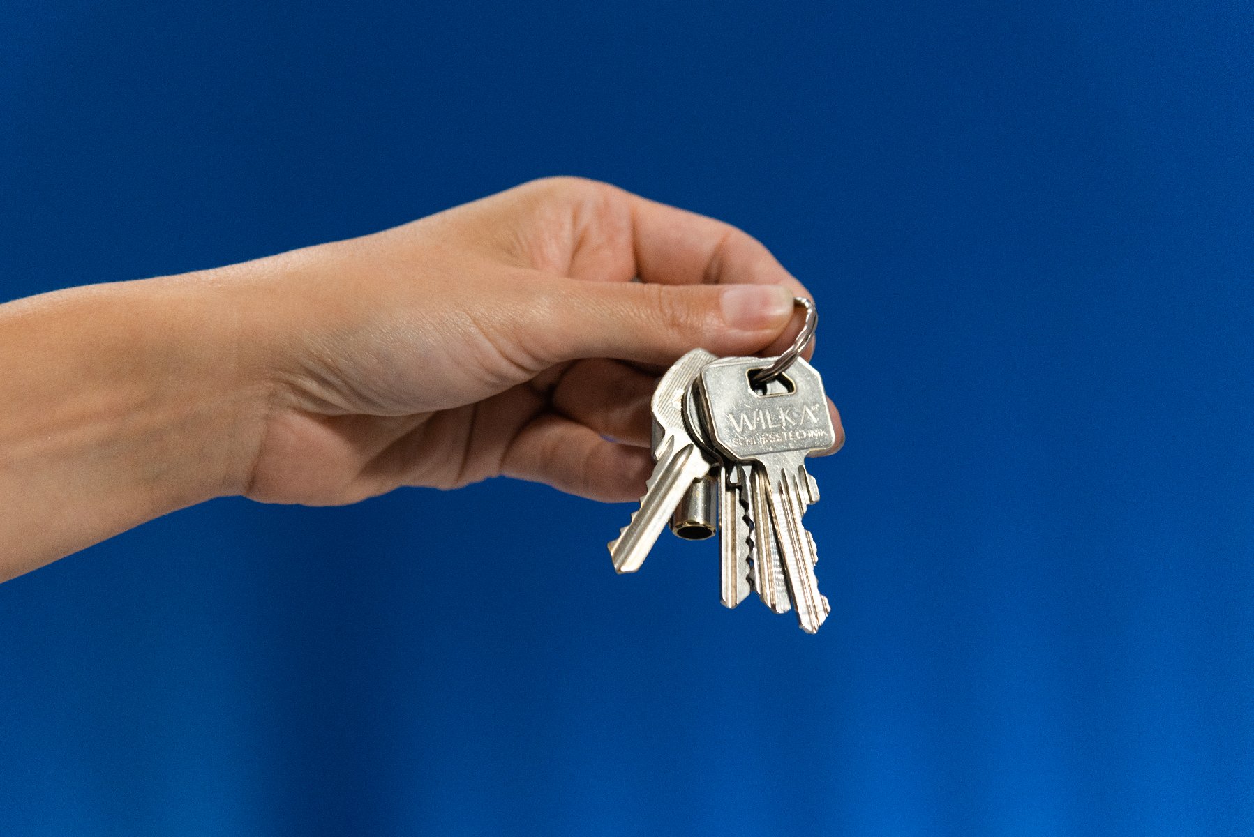 Ręka trzyma pęk metalowych kluczy na srebrnym kółku, na jednolitym niebieskim tle. - grafika artykułu