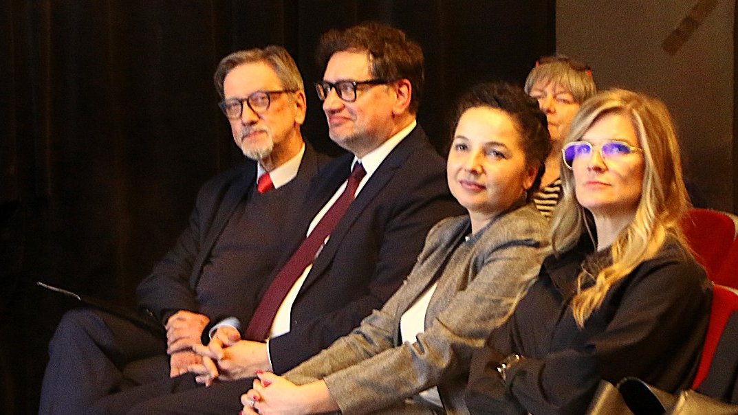Na zdjęciu widzimy osoby siedzące w I rzędzie w auli na spotkaniu.