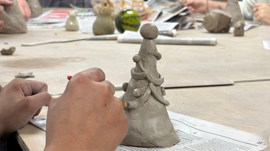 Grupa osób pracuje nad rzeźbami z gliny w jasnym, dobrze oświetlonym pomieszczeniu.