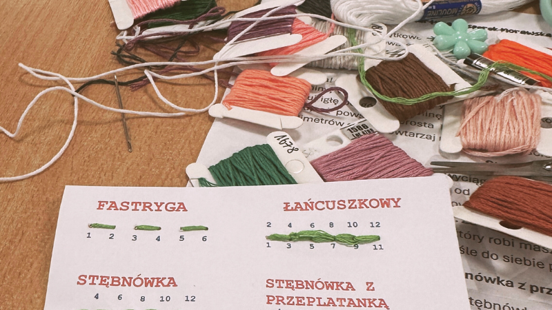Zdjęcie przedstawia rodzaje ściegów w szyciu oraz w tle nitki oraz nożyczki, zdjęcie zostało wykonane na warsztatach z haftu na ubraniach