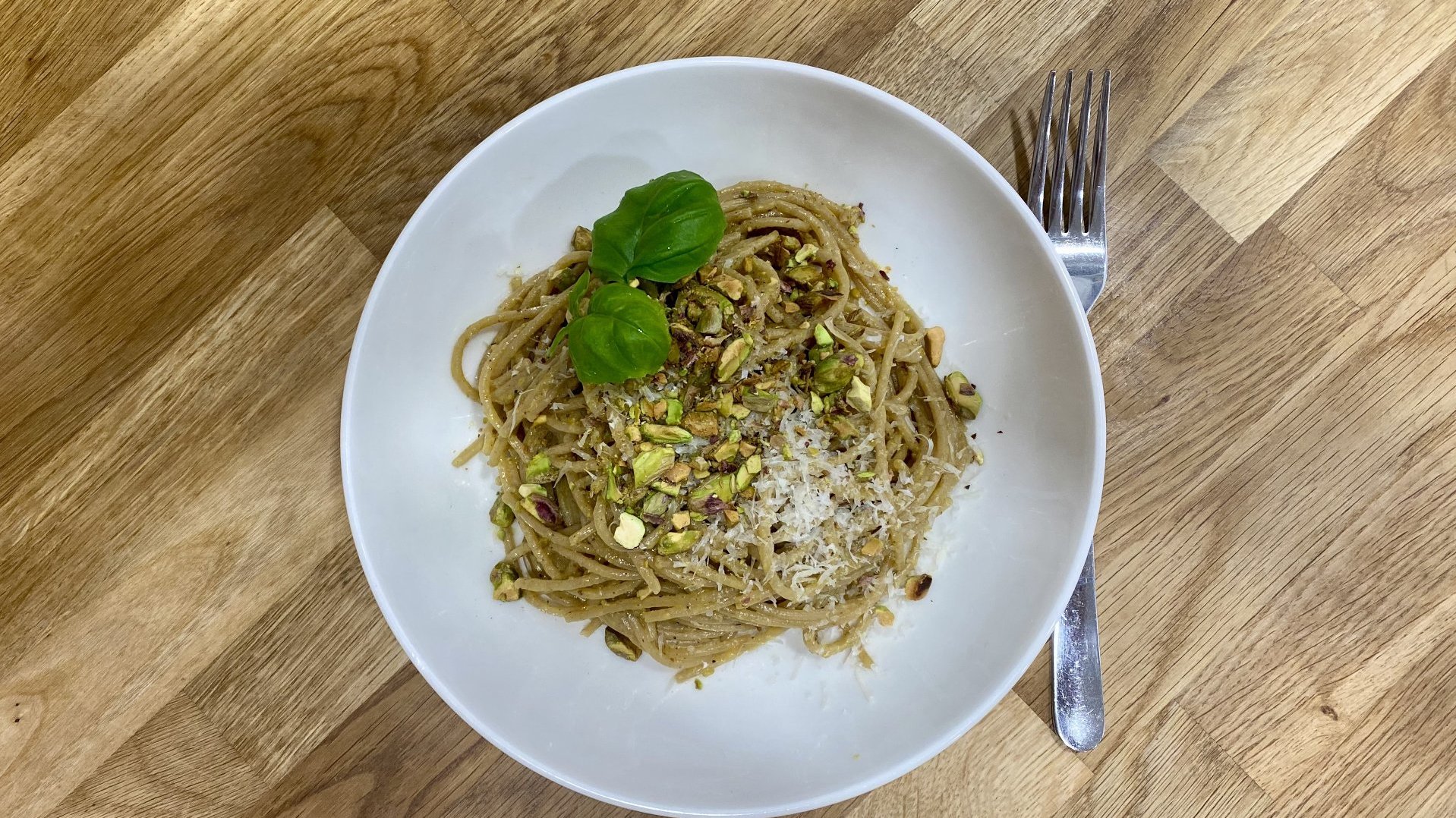 Talerz z makaronem z pistacjowym pesto, posypany pistacjami i listkami bazylii.