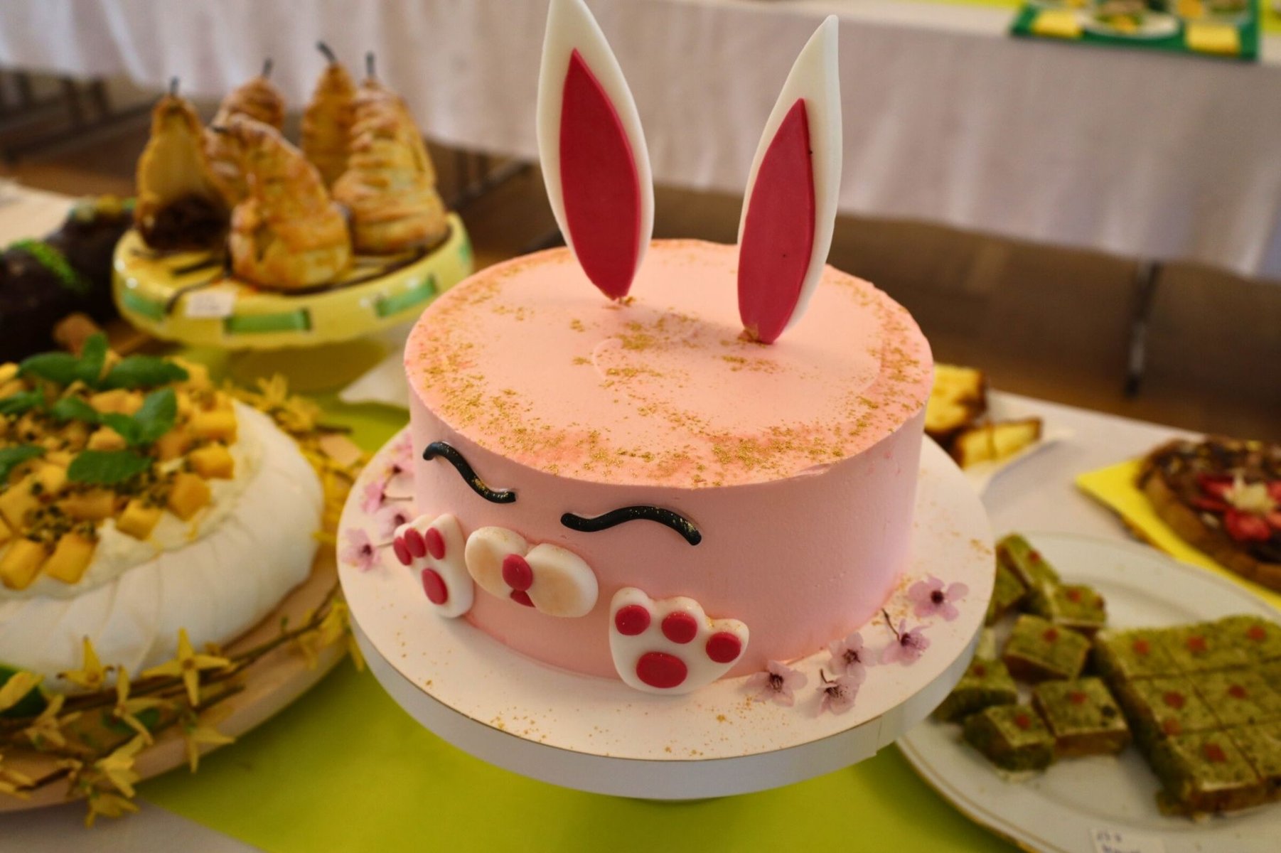 Stół zastawiony różnymi ciastami, na pierwszym planie różowy tort z króliczymi uszkami. - grafika artykułu