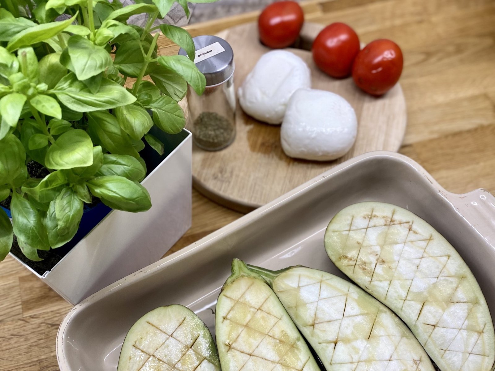 Foremka z bakłażanami naciętymi w kratkę, obok kulki mozzarelli, pomidory i bazylia. - grafika artykułu