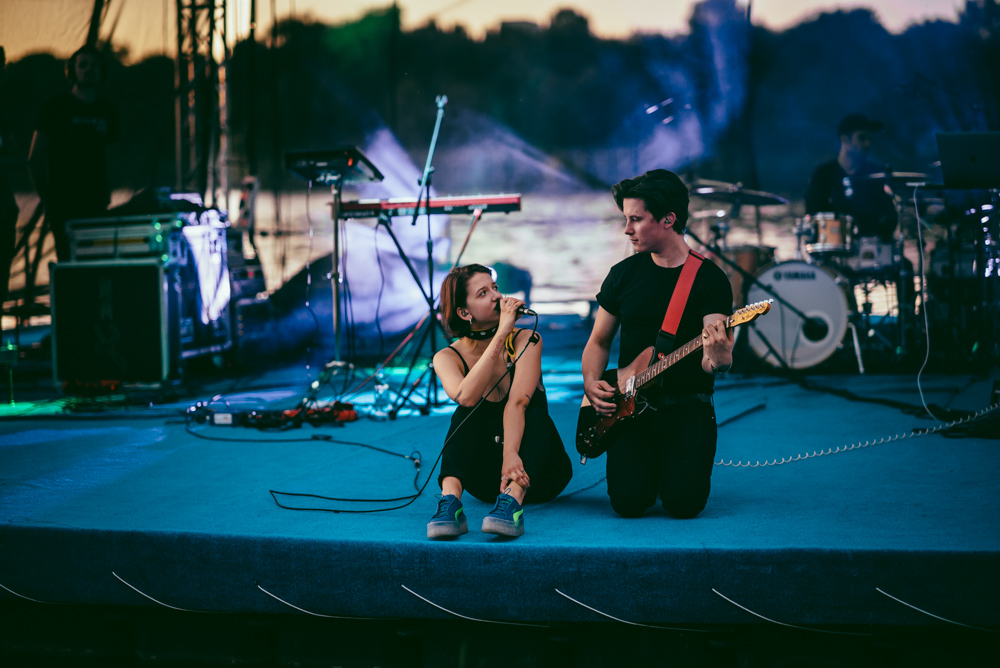 Bezpłatne koncerty, znani polscy artyści i wakacyjna atmosfera - tak zapowiada się kolejna edycja cyklu #NaFalach Plenerowy koncert muzyczny. Na scenie dwóch muzyków na pierwszym planie - jeden klęczy i gra na gitarze elektrycznej, drugi siedzi na podłodze sceny, trzyma mikrofon i śpiewa.