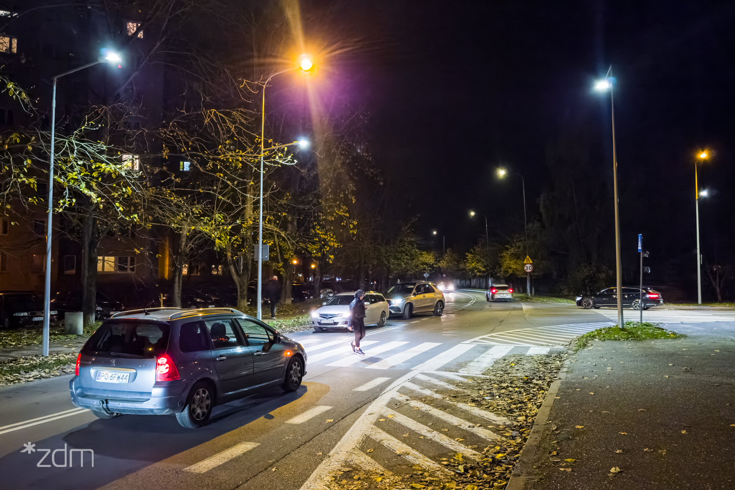 Samochody stojące przed doświetlonym przejściem, przez które przechodzi pieszy