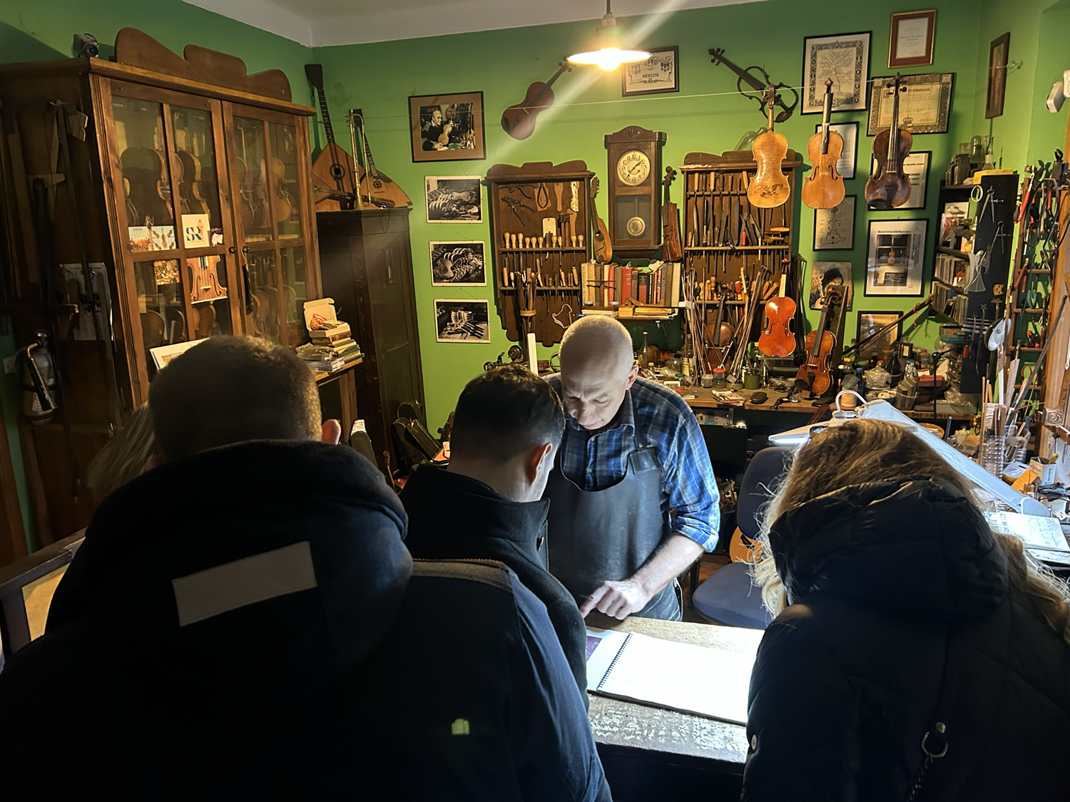 Uczestnicy wizyty studyjnej z Serbii przy stole, wspólnie oglądająca instrument muzyczny w pracowni lutniczej.