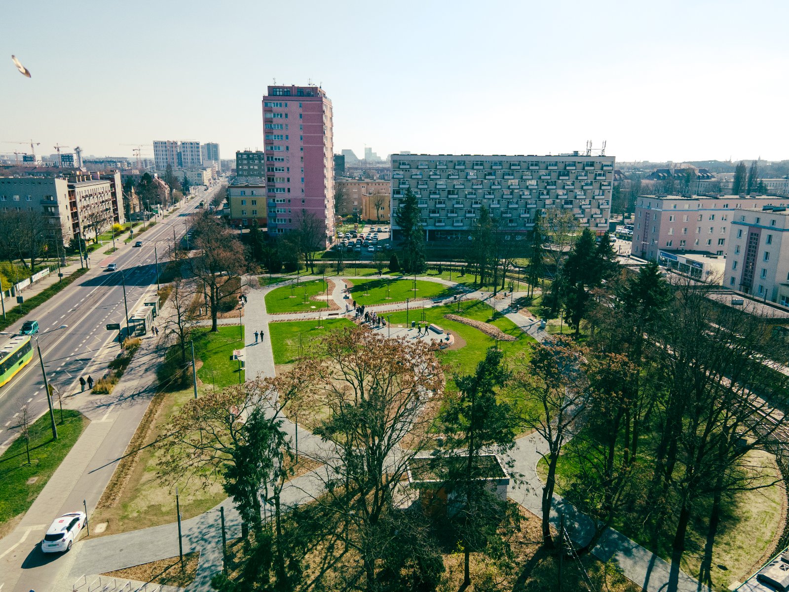 Ograniczenie sprzedaży alkoholu na Ogrodach Widok z góry na skwer na Ogrodach. W centrum zdjęcia widać zielony park z alejkami i ławkami. Po lewej stronie parku biegnie ulica z ruchem samochodowym, a po prawej stronie widoczne są bloki mieszkalne i budynki.