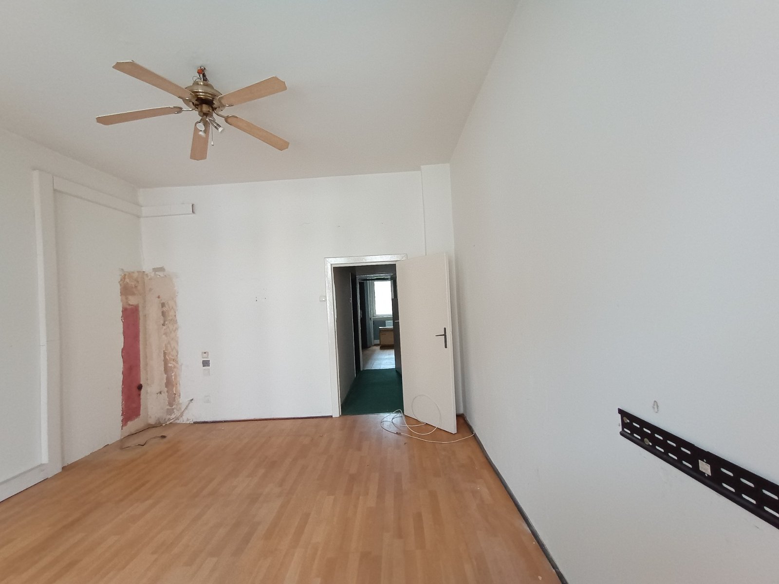 Wnętrze pokoju w mieszkaniu z nietypowymi dekoracjami. Ściany są pomalowane na kolor żółty, a wokół futryny drzwi ułożono nieregularną kompozycję z ozdobnego, piaskowego kamienia. Po lewej stronie wisi duża, ażurowa dekoracja ścienna w kształcie słońca lub zegara, a po prawej obraz nawiązujący do sztuki starożytnego Egiptu.